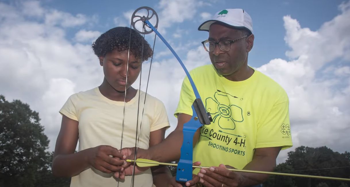 Johnny assisting instructing a student with the 4-H Club how to show a bow